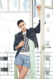 Model Nine d'Urso posing in a denim jacket and patterned knit top leaning against an open window for Dior