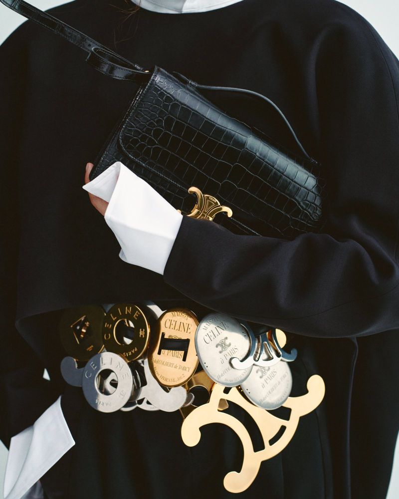 Fashion shot of a woman wearing a black outfit with a designer belt and a black alligator-skin purse with a gold logo.