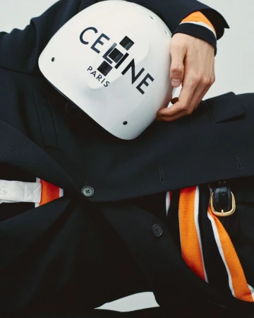 Model wearing dark coat holding white Celine branded helmet against neutral background