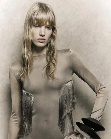 Model with blonde hair and bangs wearing a beige long-sleeved dress against a textured neutral wall for Ferragamo SS26