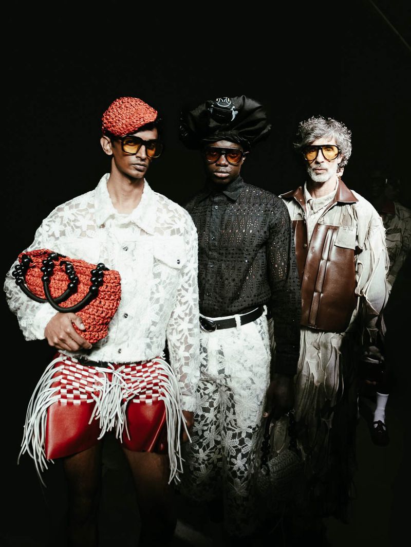 Three fashion models in patterned shirts and shorts pose in a dark studio, showing off unique and colorful outfits and accessories.
