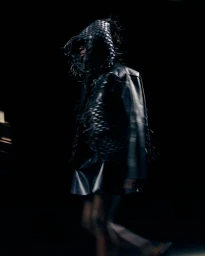 Model wearing a black woven hooded jacket and skirt walking backstage for Tokyo James