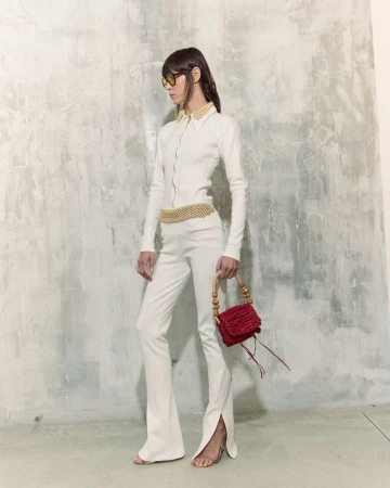 Model in white collared outfit and sunglasses holding a red textured handbag against a distressed concrete wall