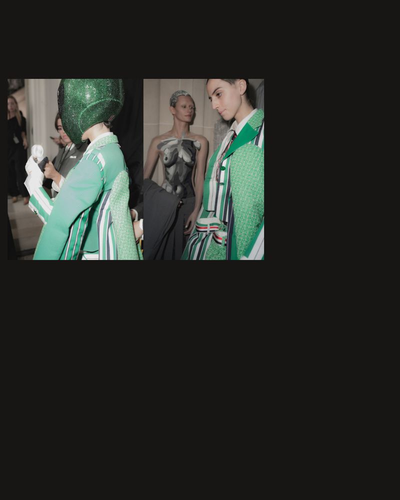 Fashion show backstage featuring models in green and white striped blazers, one with body paint, wearing a green glittery head covering.