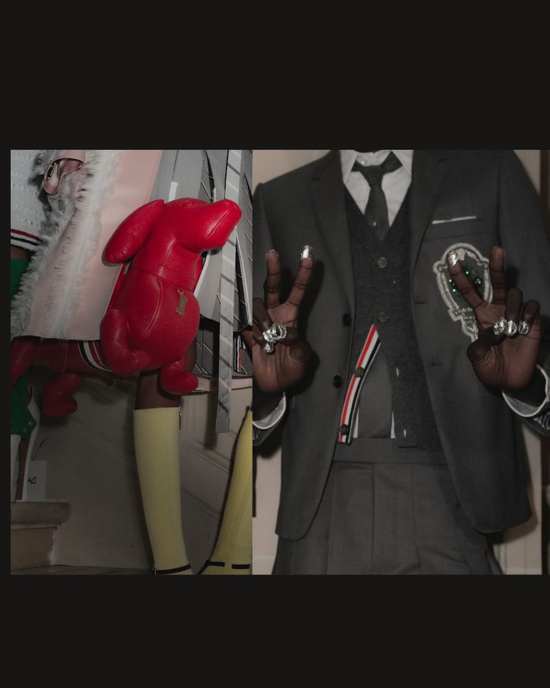 Fashion shot: Person in suit making peace sign with rings on fingers, next to mannequin holding red dog head in interior.