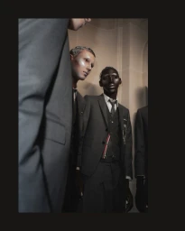 Models in tailored grey suits backstage at Thom Browne SS26 featuring dramatic theatrical makeup and structured menswear tailoring.