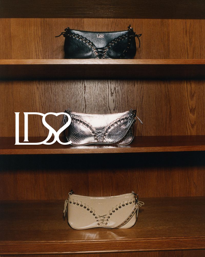 Three stylish handbags with decorative lacing displayed on wooden shelves in a well-lit, vertical product shot. Fashion accessories.