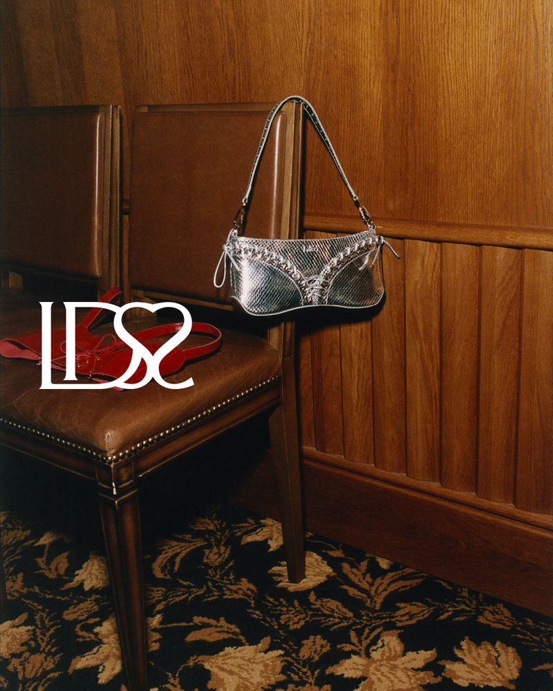 Silver metallic handbag hanging near a leather chair with red accessories. Floral pattern carpet, wood paneling in the background.