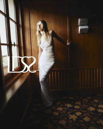 Paige Reifler in a white halter dress standing near a wooden wall and window for Ludovic de Saint Sernin S/S 25.