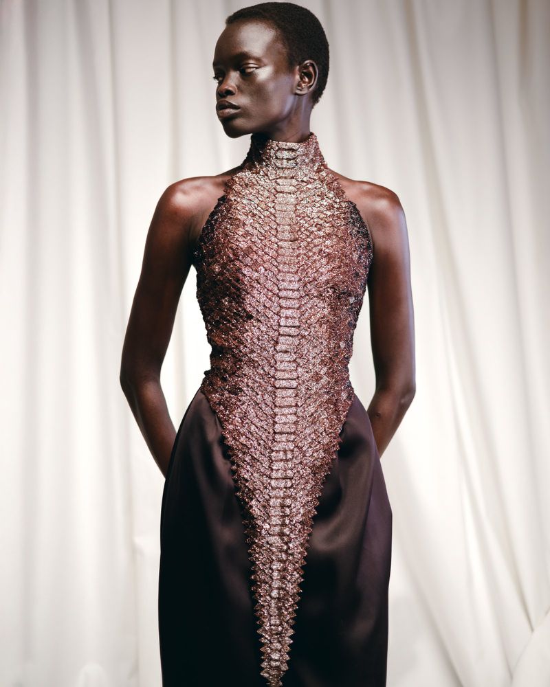 Fashion shot of an African female model in a snakeskin-textured halter dress against a white fabric background in soft, diffused lighting.