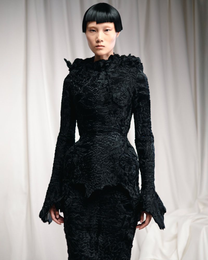 Elegant Asian woman in runway fashion show.  Black textured couture dress with ruffles, full sleeves and fitted skirt. Indoor portrait with white backdrop.