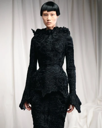 Elegant Asian woman in runway fashion show.  Black textured couture dress with ruffles, full sleeves and fitted skirt. Indoor portrait with white backdrop.