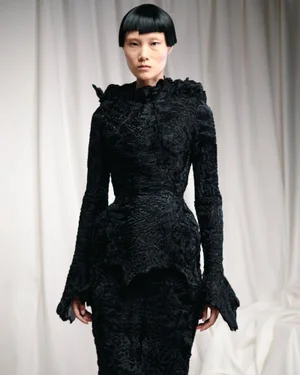 Model in textured black haute couture dress standing against draped white fabric backdrop by Ashi Studio
