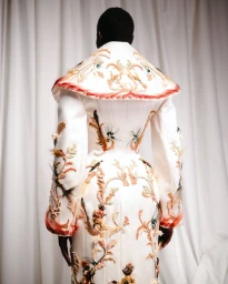 Model seen from behind wearing an ornate white couture coat with intricate embroidered and feathered patterns.