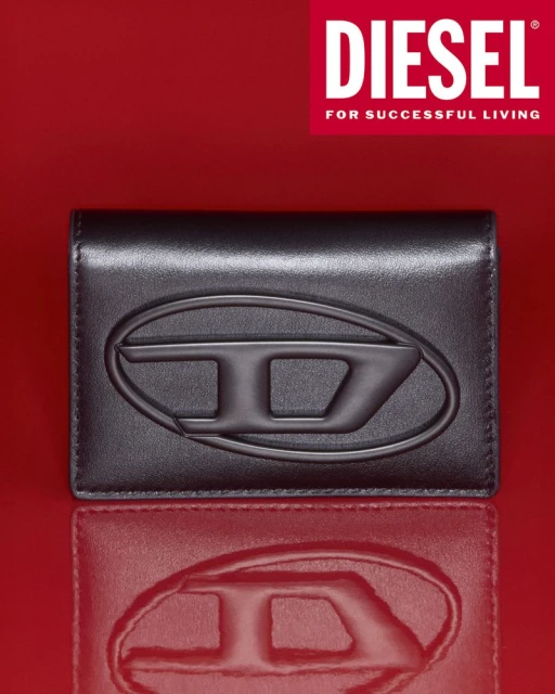 Studio shot of a black leather card holder with a prominent embossed logo, reflecting on a red surface, with the DIESEL logo above.