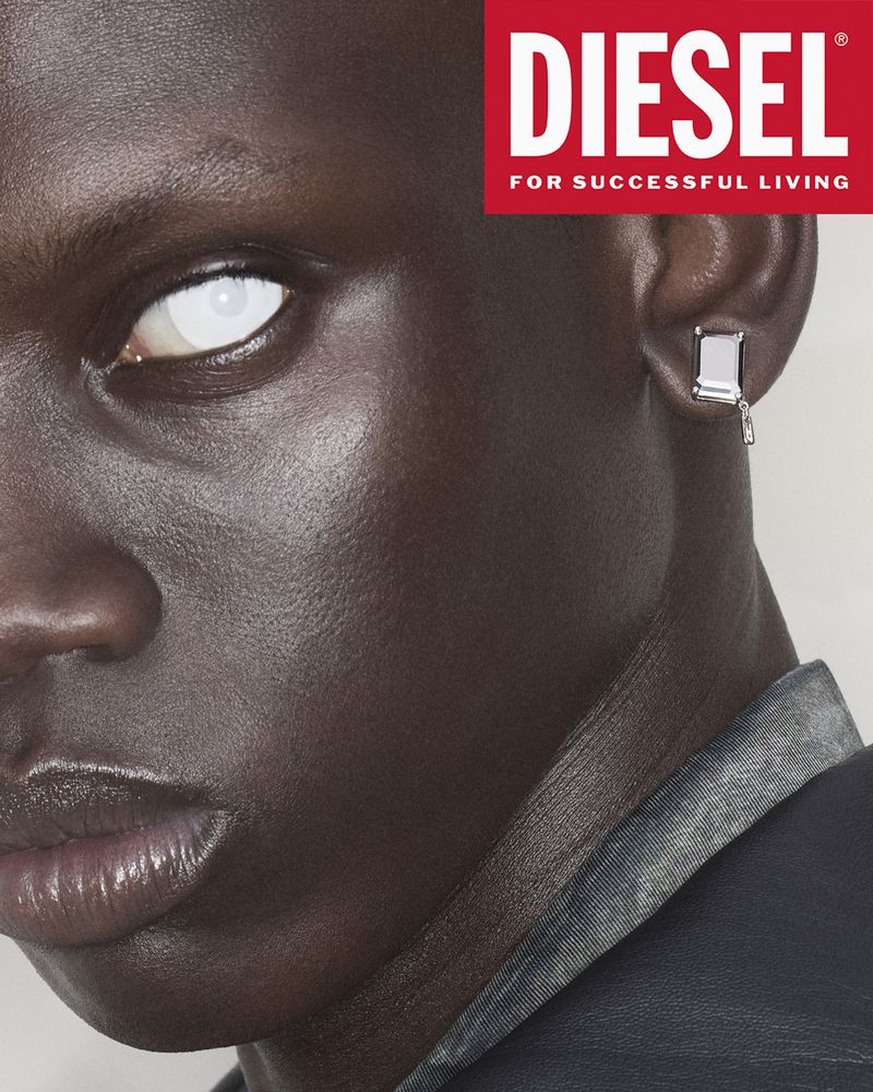 Close-up studio shot of a dark-skinned adult male model with white contact lenses and a silver earring, wearing a dark denim jacket.