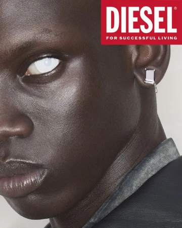 Close-up studio shot of a dark-skinned adult male model with white contact lenses and a silver earring, wearing a dark denim jacket.
