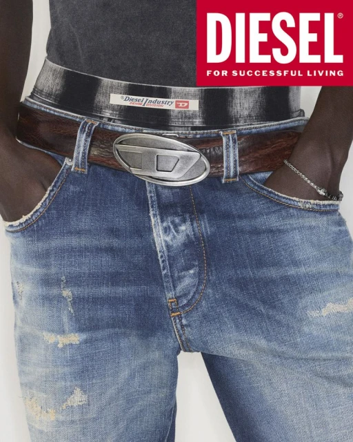 Close-up of denim jeans on an adult with a brown leather belt featuring a Diesel logo buckle and Diesel brand text at the top.
