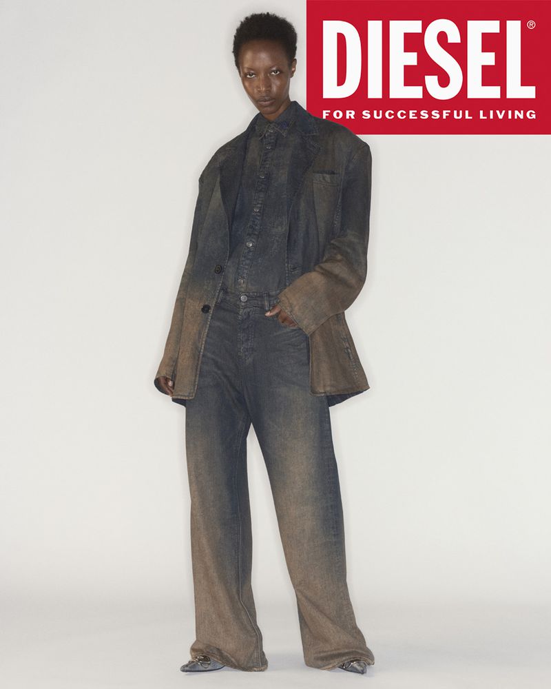 An adult woman in a denim jacket and wide-leg jeans stands in front of a logo. The clothing is denim with distressed, ombre coloring.