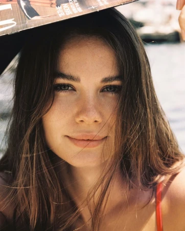 Close-up portrait of a woman with long brown hair holding a magazine above her head under natural sunlight.