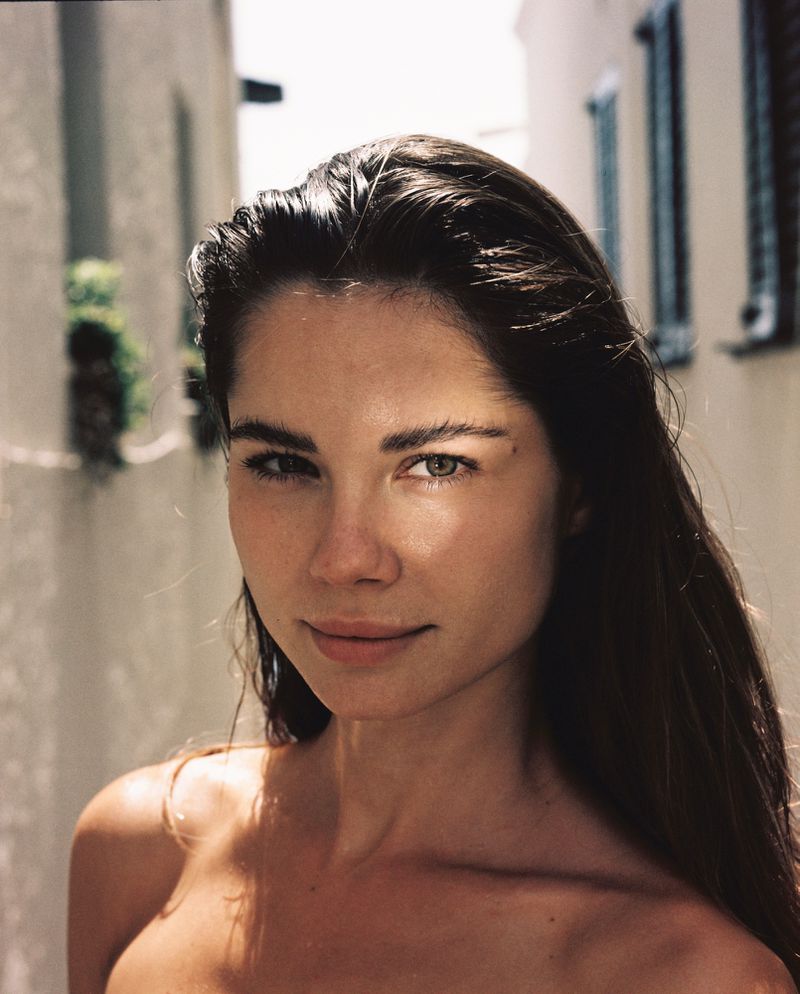 Portrait of a woman with brown hair in an outdoor setting with natural lighting, showcasing a minimalist aesthetic and focus on facial features.