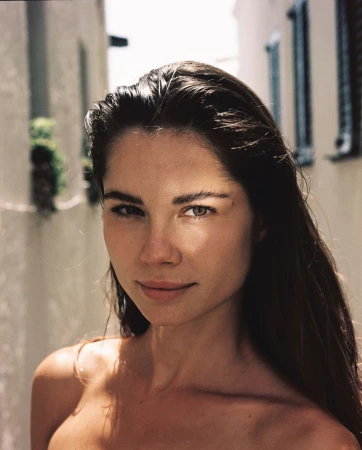 Portrait of a woman with brown hair in an outdoor setting with natural lighting, showcasing a minimalist aesthetic and focus on facial features.