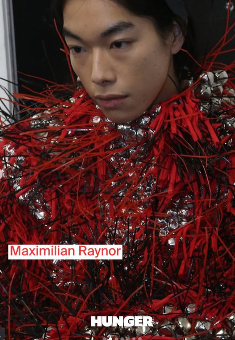 Close-up studio portrait of a young Asian male model wearing a unique, fringed red and silver top for a fashion editorial.