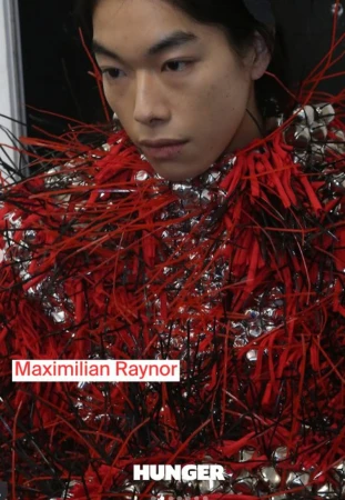 Close-up studio portrait of a young Asian male model wearing a unique, fringed red and silver top for a fashion editorial.