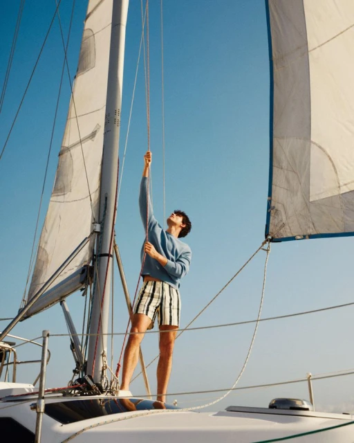Young man on a sailboat pulls ropes while sailing on the water under a clear blue sky on a sunny day. Maritime sport and recreation.