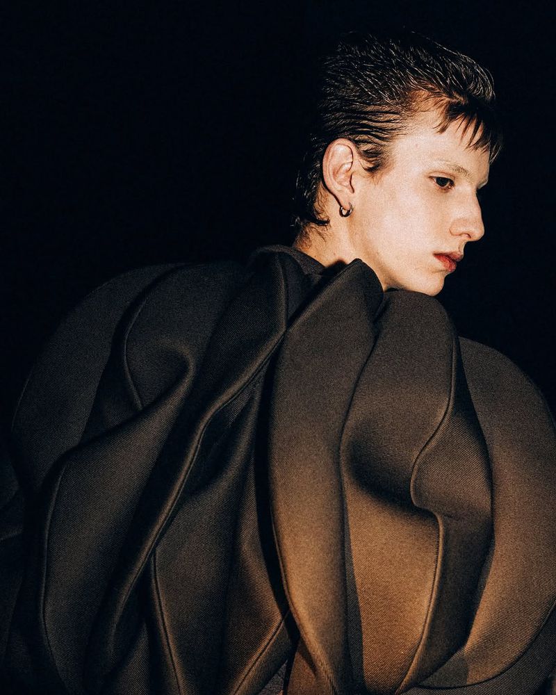Person wearing sculptural garment against a dark background, stylish and unusual fashion, close-up shot with interesting form and textures.