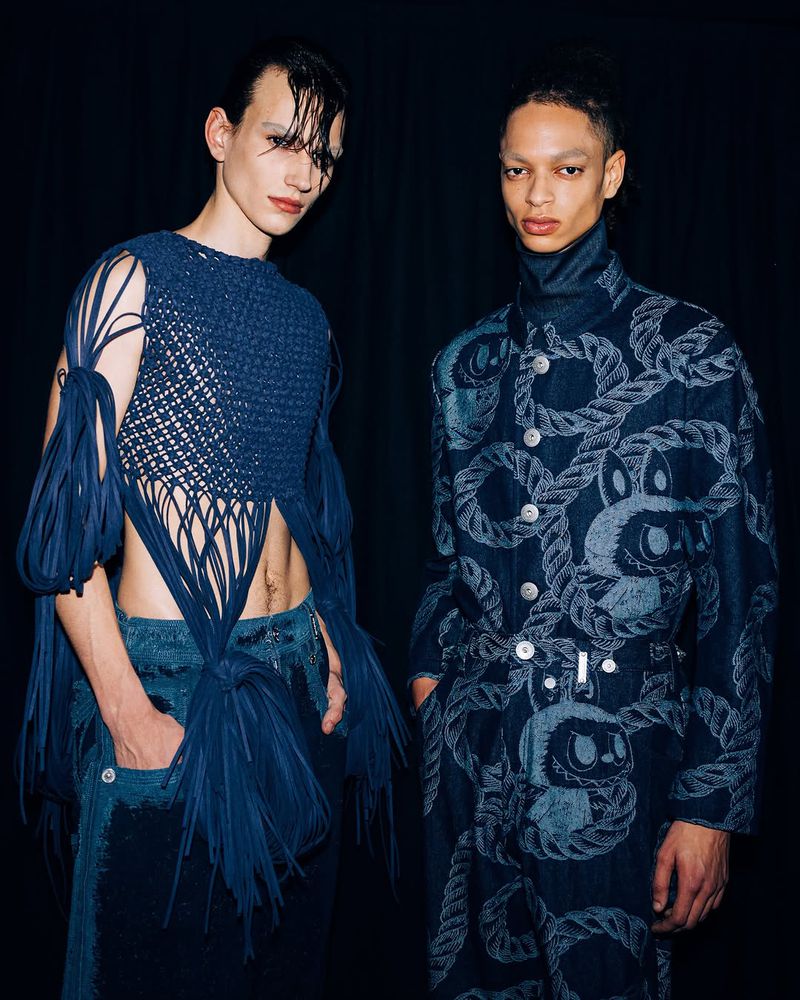 Two fashion models in a studio setting wearing blue-toned outfits, one a knit crop top and the other a rope-printed suit.