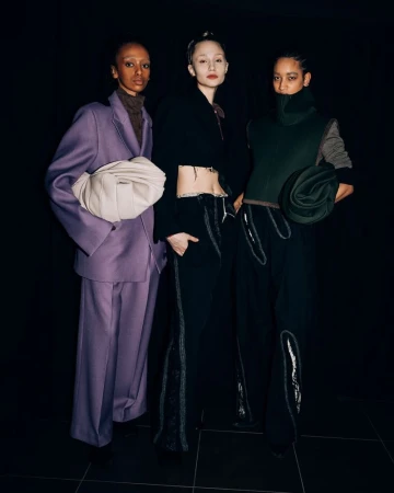 Three fashion models pose indoors against a dark background, showcasing avant-garde clothing with unique textures and designs.