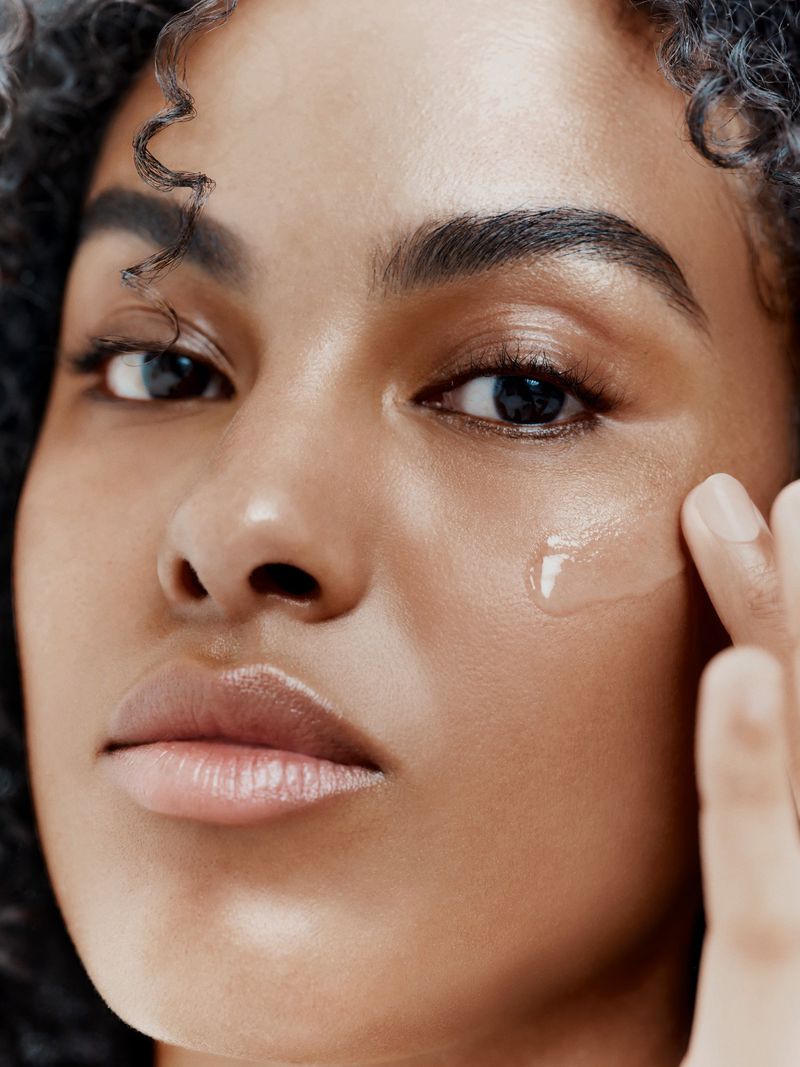 Close-up studio shot of a woman applying clear serum to her face. The focus highlights skin hydration and healthy skincare practices.