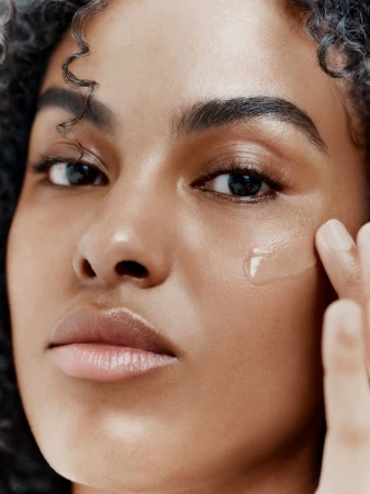 Close-up portrait of a model applying a clear serum to her cheek for Augustinus Bader by Jack Grange.