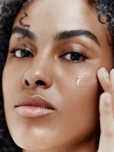 Close-up portrait of a model applying a clear serum to her cheek for Augustinus Bader by Jack Grange.