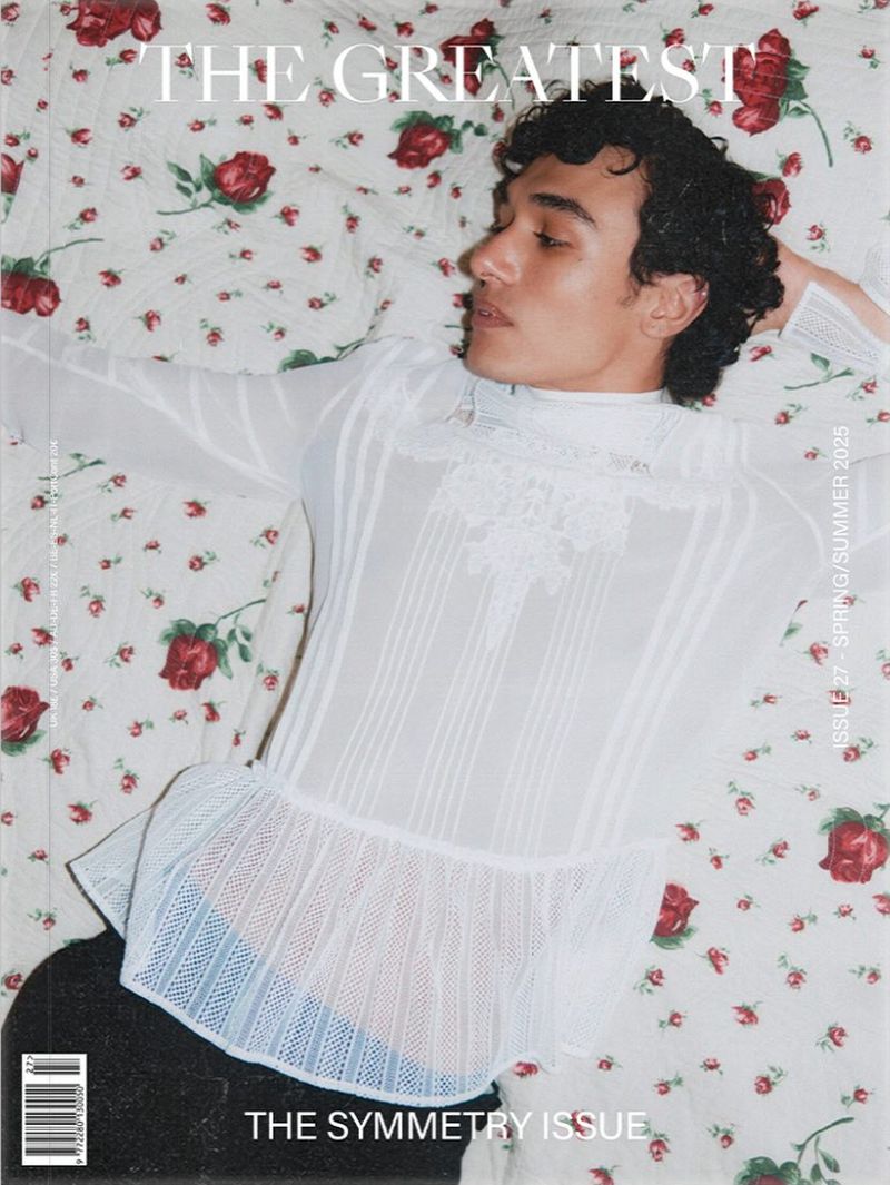 Fashion magazine cover featuring a reclining person with curly dark hair wearing a frilly, see-through white blouse on a floral bedspread.