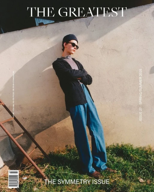 Magazine cover featuring a male model in blue pants, black jacket, and sunglasses leaning against a textured wall outdoors.