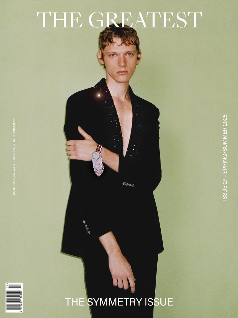 Fashion magazine cover featuring a young adult male model in a black suit and unique accessory against a light green backdrop.