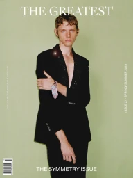 Young man in a black blazer with lapel embellishments against a plain light green background for magazine cover