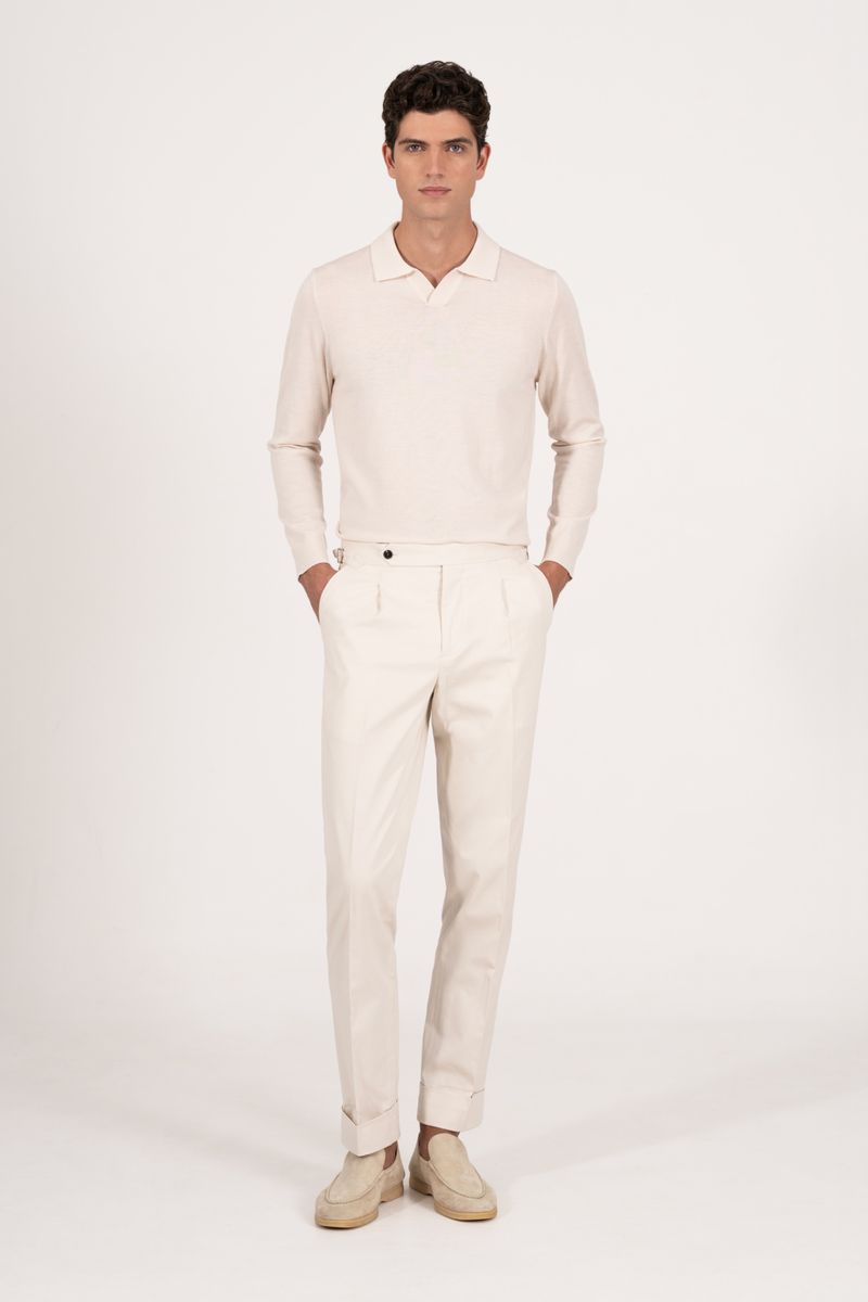 Full-length shot of a dark-haired man in a polo-style shirt, light-colored pants, and moccasins posing in a brightly lit photo studio.