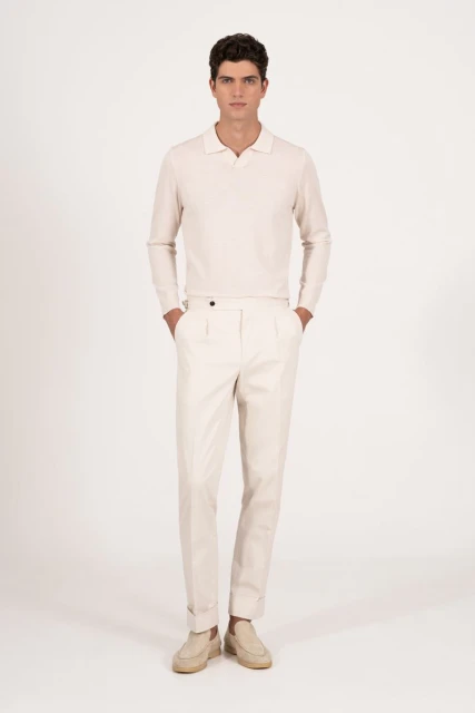 Full-length shot of a dark-haired man in a polo-style shirt, light-colored pants, and moccasins posing in a brightly lit photo studio.