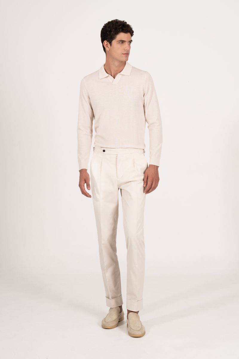 A full-length studio shot of a young adult man in a light cream-colored polo shirt, matching pants, and light beige shoes, looking away.