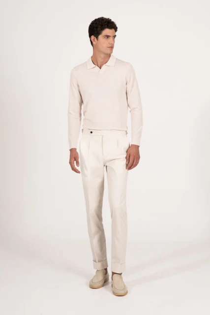 A full-length studio shot of a young adult man in a light cream-colored polo shirt, matching pants, and light beige shoes, looking away.