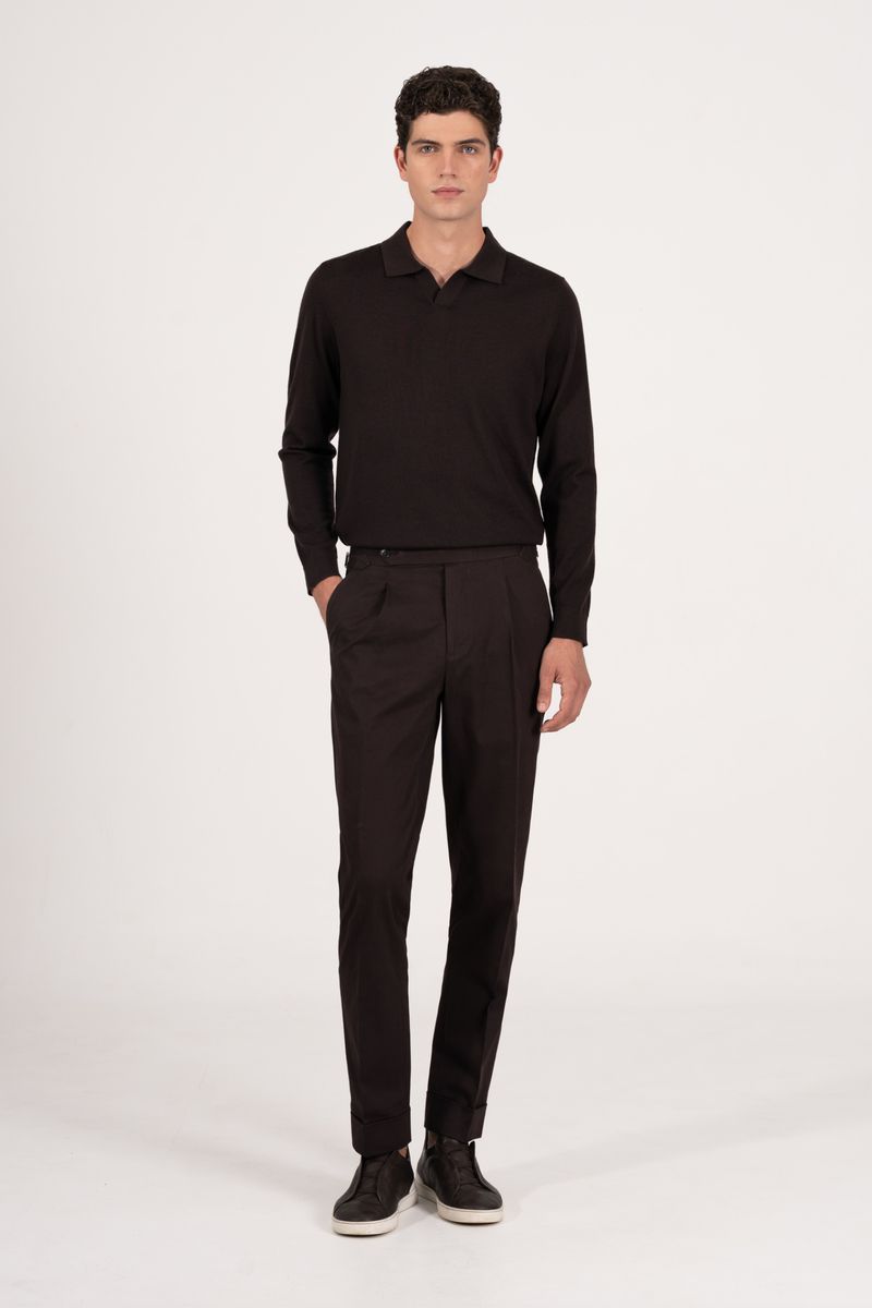 A full-length shot of a brunette male model in a long-sleeved, dark polo shirt and dark dress pants posing against a neutral backdrop.