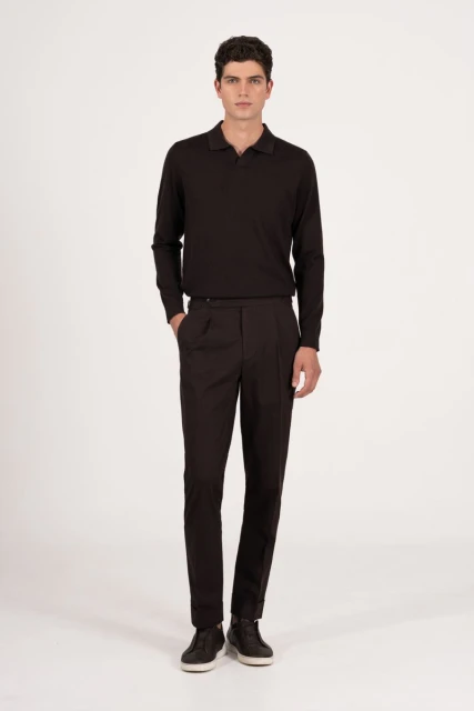 A full-length shot of a brunette male model in a long-sleeved, dark polo shirt and dark dress pants posing against a neutral backdrop.