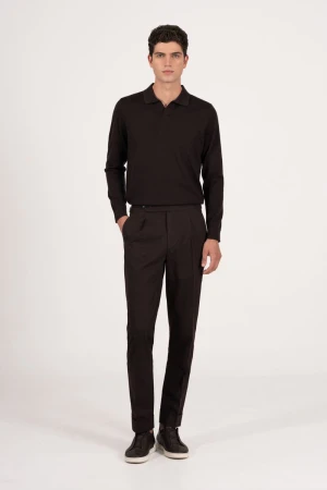 A full-length shot of a brunette male model in a long-sleeved, dark polo shirt and dark dress pants posing against a neutral backdrop.