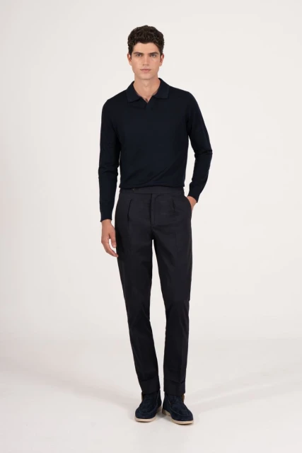 Full-length studio shot of a male model in a navy blue long-sleeved polo shirt and pleated trousers posing against a white backdrop.