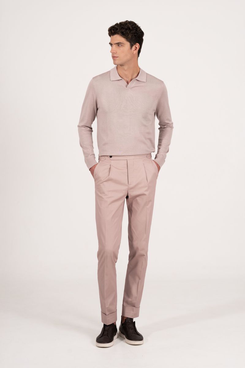 Full-length portrait of an adult male model in a pale pink collared sweater and matching tailored trousers with a neutral background.