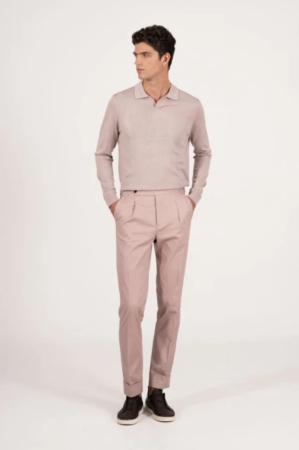 Full-length portrait of an adult male model in a pale pink collared sweater and matching tailored trousers with a neutral background.