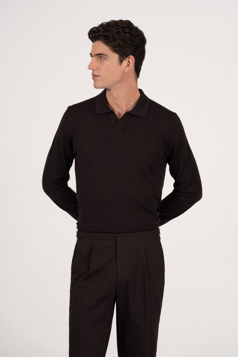 A man wearing a dark, long-sleeve polo shirt and pleated trousers poses against a neutral backdrop, looking to the side in a studio shot.
